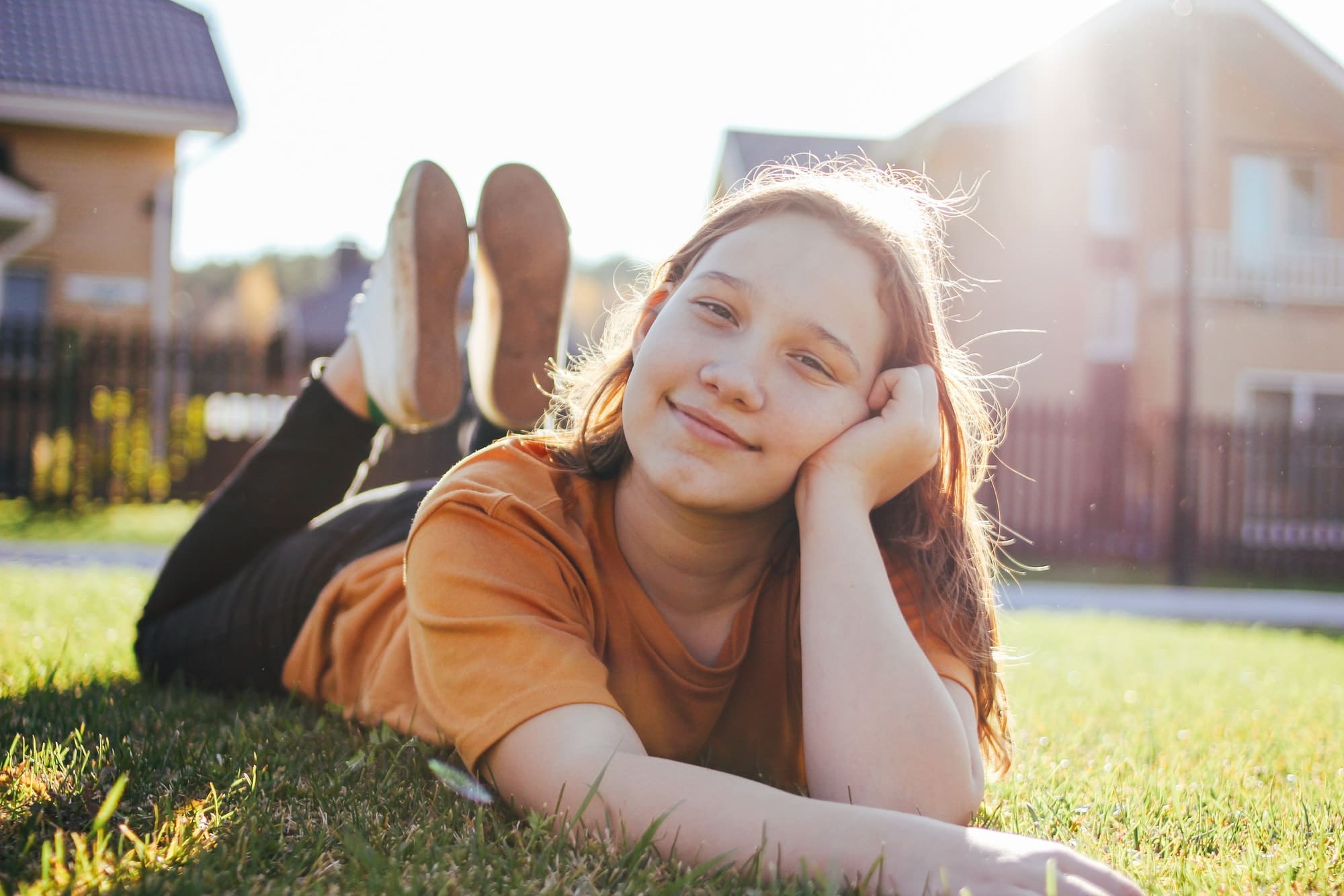 Portrait of smiling teen girl lying on sunny green grass of cottage village on the background